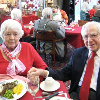 An elderly couple holding hands while dining at a restaurant.