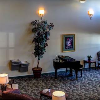 A cozy lobby area with a grand piano, seating, indoor plants, and decorative wall art.
