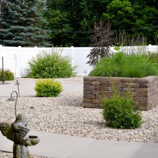 A neatly landscaped garden featuring a brick planter, decorative statue, and gravel ground cover.