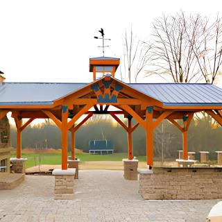 A wooden pavilion set in a park landscape, featuring a weathervane on top.