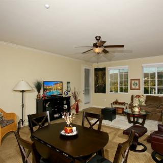 A cozy living room with a dining area, featuring comfortable seating, a television, and large windows.