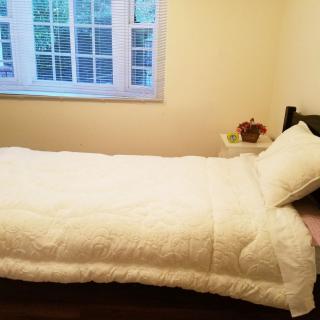 A neatly made bed with white bedding in a cozy bedroom facing a window.
