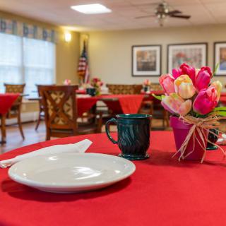 A cozy dining area with tables covered in red cloths, adorned with floral centerpieces and place settings.