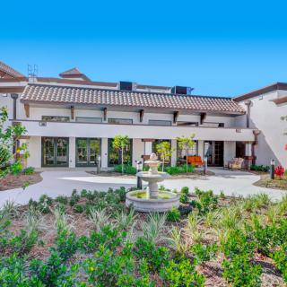 A beautiful courtyard view of a house with a garden and fountain on a sunny day.