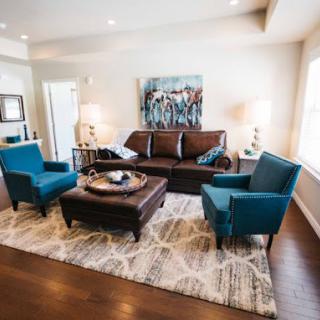 A well-designed living room featuring a brown sofa, blue armchairs, a central coffee table, and decorative elements.