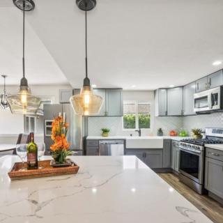 A modern kitchen with gray cabinets, stainless steel appliances, and pendant lighting.