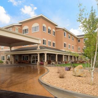 A modern multi-story building with a landscaped entrance and clear sky.