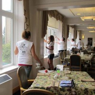 A group of volunteers cleaning windows in a community room.