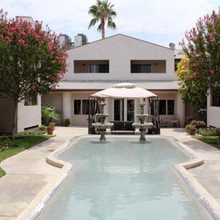 A modern house with a swimming pool and fountain in the foreground, surrounded by lush trees.