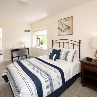 A cozy bedroom with a striped bedspread, a nightstand with a lamp, and a desk near the window.