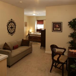 A cozy interior featuring a small living area with a sofa and chair, leading into a bedroom.