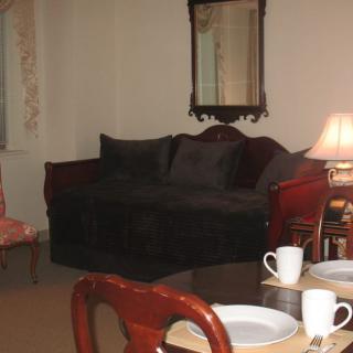A cozy living room with a sofa, mirror, dining table set with cups, and a lamp.