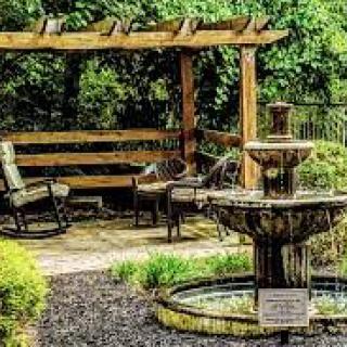 A tranquil garden with a fountain, wooden pergola, and seating area.