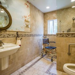 An accessible bathroom featuring a wheelchair, tiled walls, a sink, and a toilet.