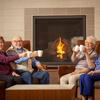 A group of seniors enjoying hot drinks in front of a cozy fireplace.