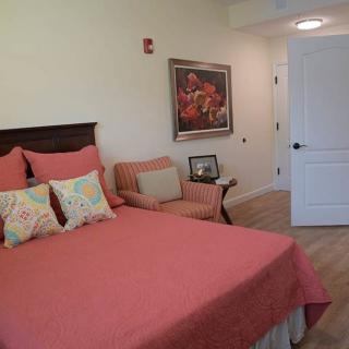 A cozy bedroom with a bed dressed in coral bedding, an armchair, and wall decor.