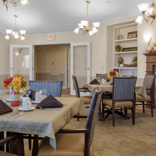 A cozy dining room with neatly arranged tables and chairs, adorned with elegant chandeliers.