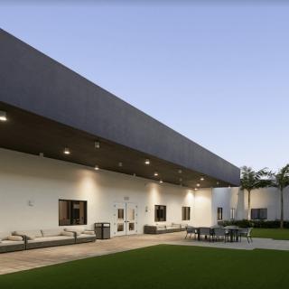 A modern building with a minimalist design featuring outdoor seating and a well-maintained lawn under the evening sky.