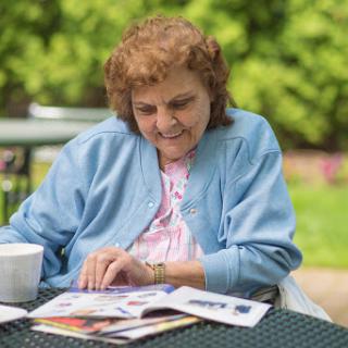 An elderly woman enjoying a peaceful moment outdoors while reading a magazine.