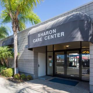 Entrance of Sharon Care Center with palm trees and a sunny sky.