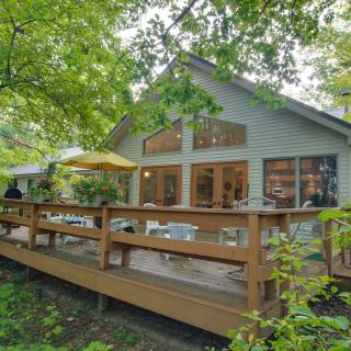 A cozy house surrounded by trees, featuring a wooden deck with outdoor seating.