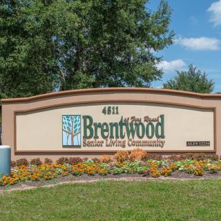 Entrance sign for Brentwood Senior Living Community surrounded by landscaped flowers and trees.