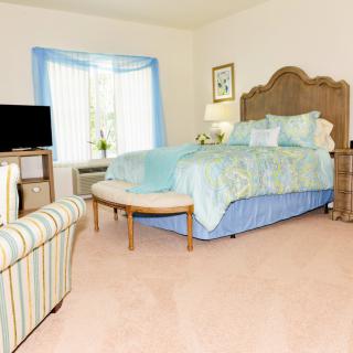 A cozy bedroom with blue accents, featuring a bed, television, and a large window.