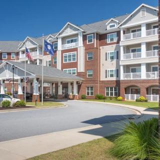 A multi-story residential building with balconies and flags at the entrance on a clear, sunny day.