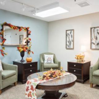 A cozy living room decorated with autumn-themed accessories, featuring armchairs, a coffee table, and wall art.