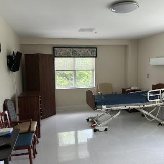 A bright and clean hospital patient room featuring a bed, furniture, and a window.
