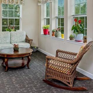 A cozy sunroom with a wicker rocking chair, a sofa, and a coffee table, decorated with potted plants by the windows.