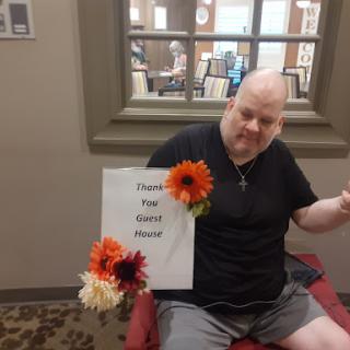 A person is sitting in a cozy indoor space, holding a sign decorated with vibrant flowers.