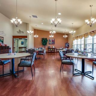 A spacious dining room with elegant chandeliers, multiple tables and chairs, featuring wood flooring and large windows.