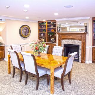 A well-appointed dining room featuring a wooden table and upholstered chairs, with decorative elements such as a fireplace and bookshelves.