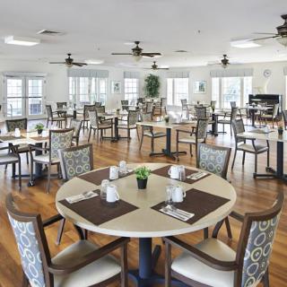 A spacious and elegantly designed dining area with multiple tables and chairs, featuring wooden flooring and large windows.