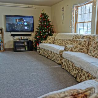 Cozy living room with a floral sofa and a festive Christmas tree, facing a mounted television.