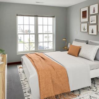 A modern and minimalist bedroom with a cozy orange accent blanket and ample natural light.