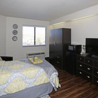 A modern bedroom with a neatly made bed, dresser, and TV.