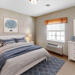 A cozy bedroom with a neatly made bed, wall art, and natural light coming through the window.