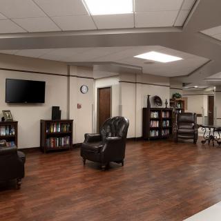 A spacious lounge area featuring leather armchairs, a television, and bookshelves on a polished wood floor.