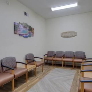 An empty waiting room with several chairs lined up against the walls.