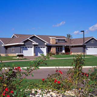 A charming suburban home with a well-manicured lawn and blooming flowers under a clear blue sky.
