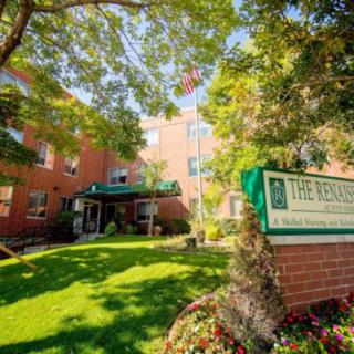 A brick building with a green entrance canopy and surrounding trees and grass, featuring a sign at the front.