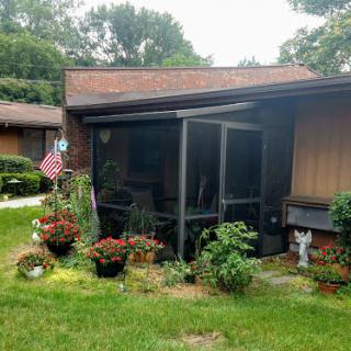A charming house with a beautifully landscaped garden and a screened porch adorned with vibrant flowers.