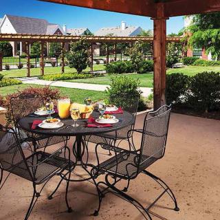 A beautifully landscaped patio with a dining set overlooking a garden and pergola on a sunny day.
