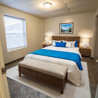 A serene and stylish bedroom featuring a comfortable bed with blue accents, framed artwork, and warm lighting.