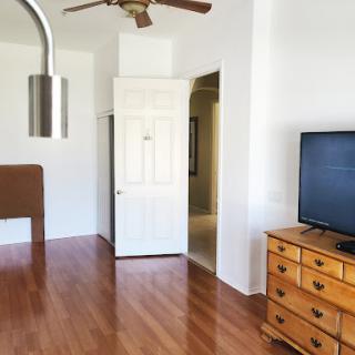 A bright and cozy living room featuring wooden floors, a TV, and a ceiling fan.
