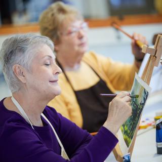 Two senior women focused on painting in an art class.