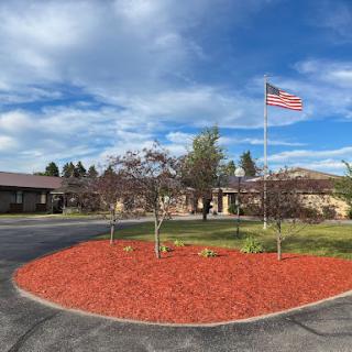 A beautifully landscaped area featuring a building, American flag, and freshly mulched flower beds under a clear blue sky.