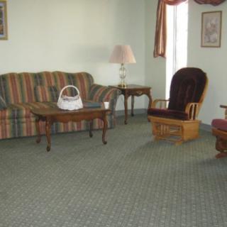 A cozy living room featuring a striped sofa, wooden coffee table, armchair, and a lamp, with light green walls and carpet flooring.